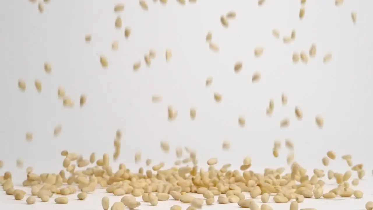 Ivory pine nuts raining down on white back drop and bouncing into a pile in slow motion