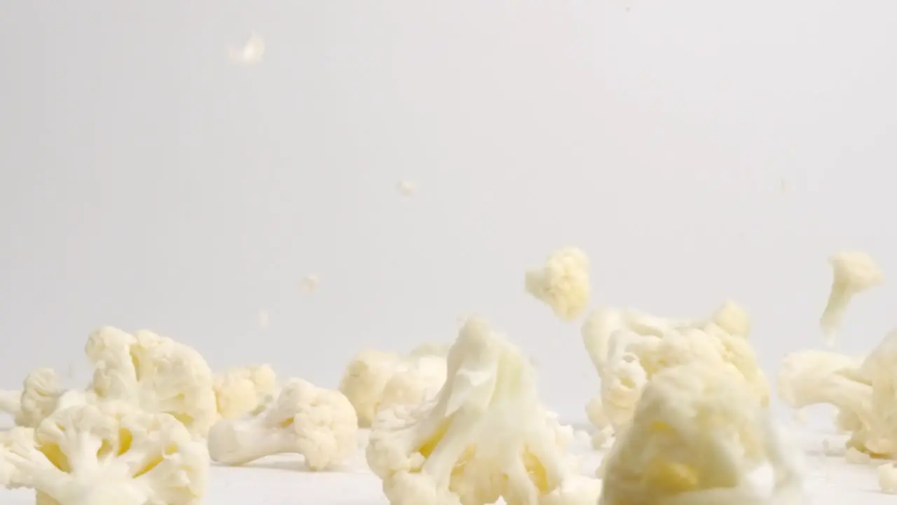 White cauliflower pieces florets bouncing on white table top in slow motion