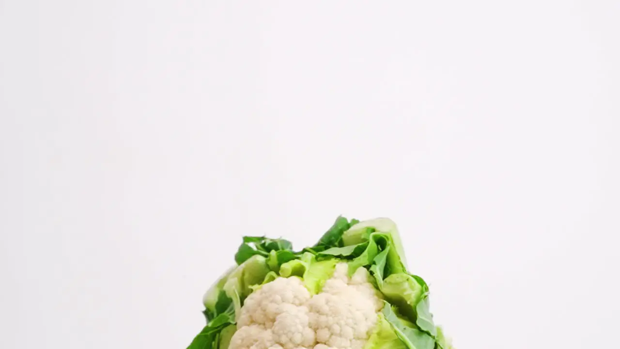 Whole head of fresh cauliflower wrapped in green leaves falling through the air in slow motion on white backdrop