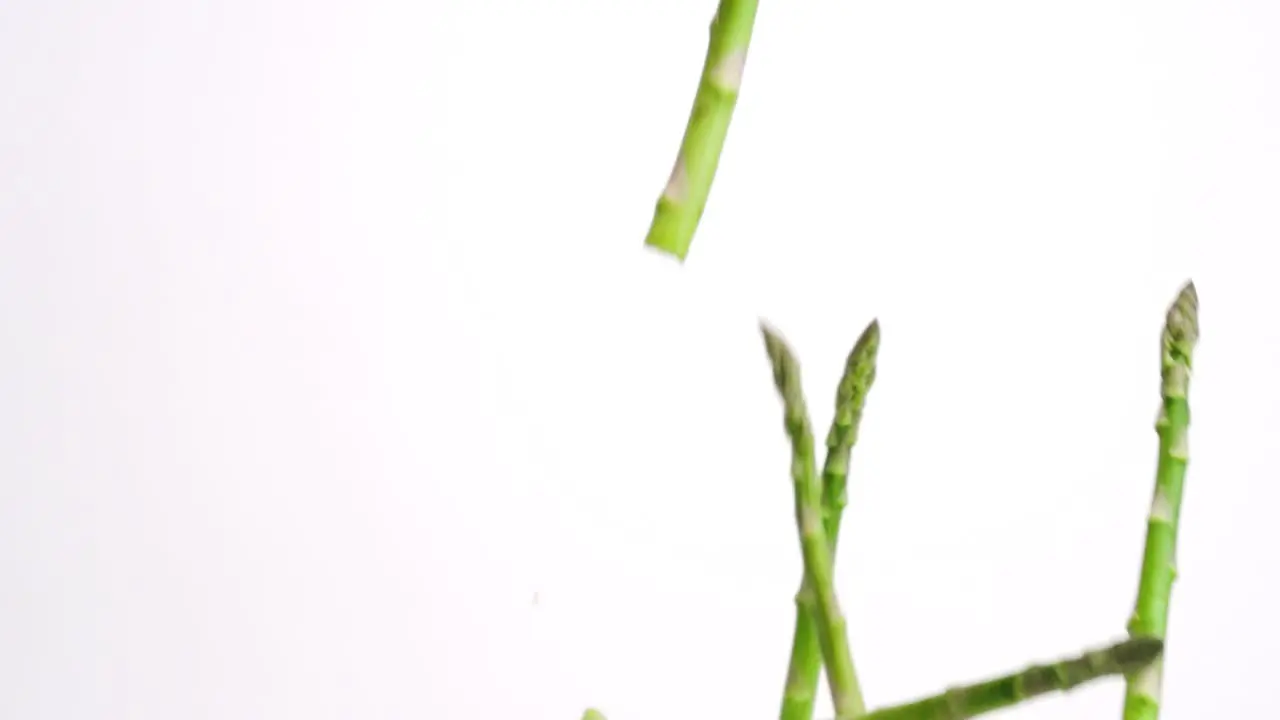 Aspragus stalks falling in slow motion and bouncing on white backdrop