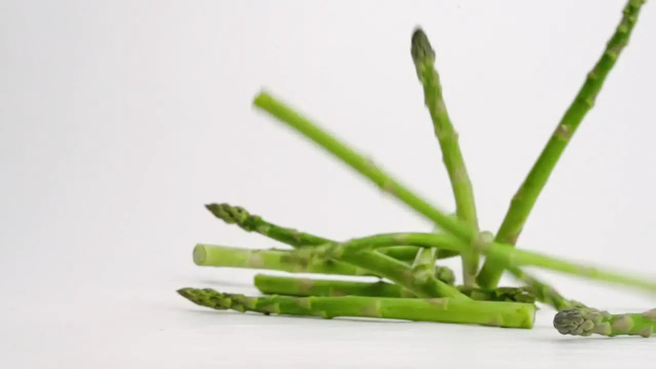 Asparagus stalks individually falling and bouncing on white backdrop in slow motion in 4k