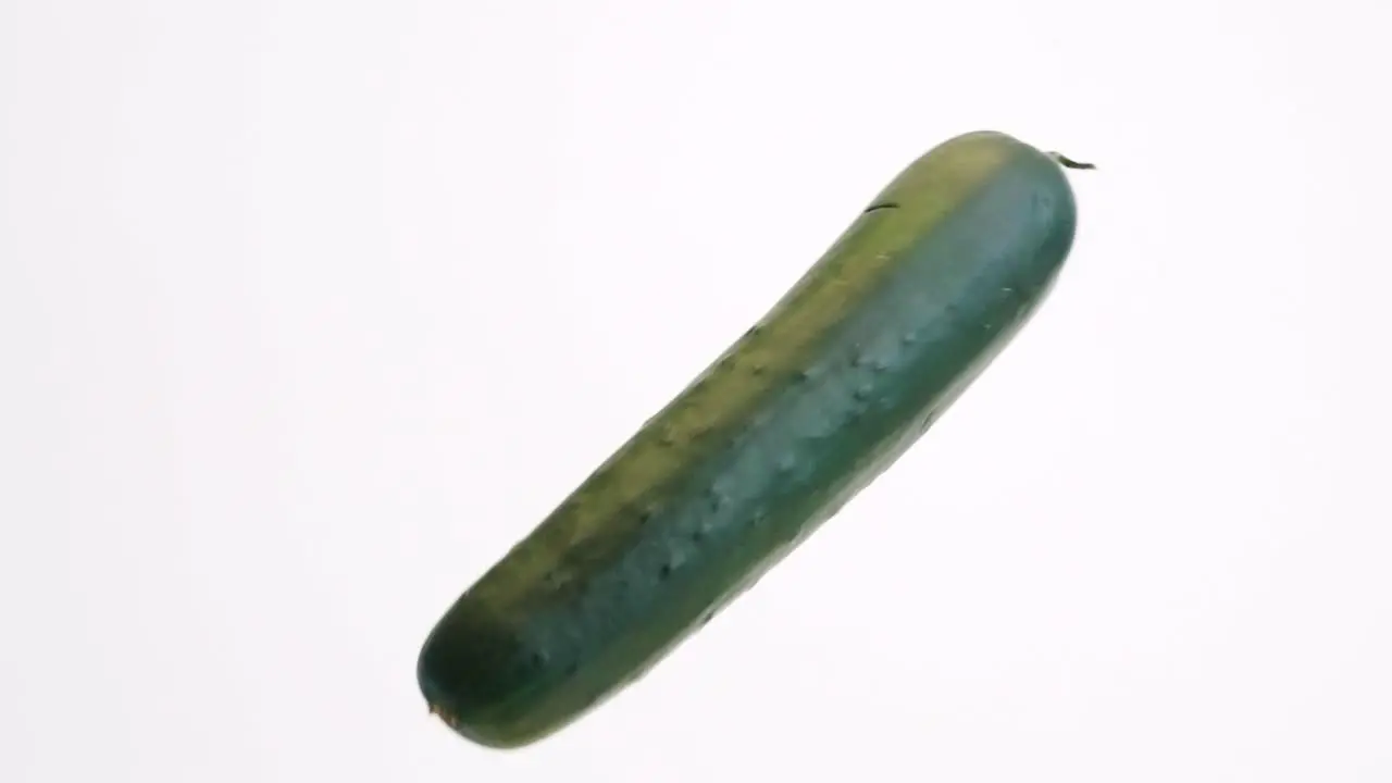 Large green whole cucumbers bouncing on white backdrop in slow motion