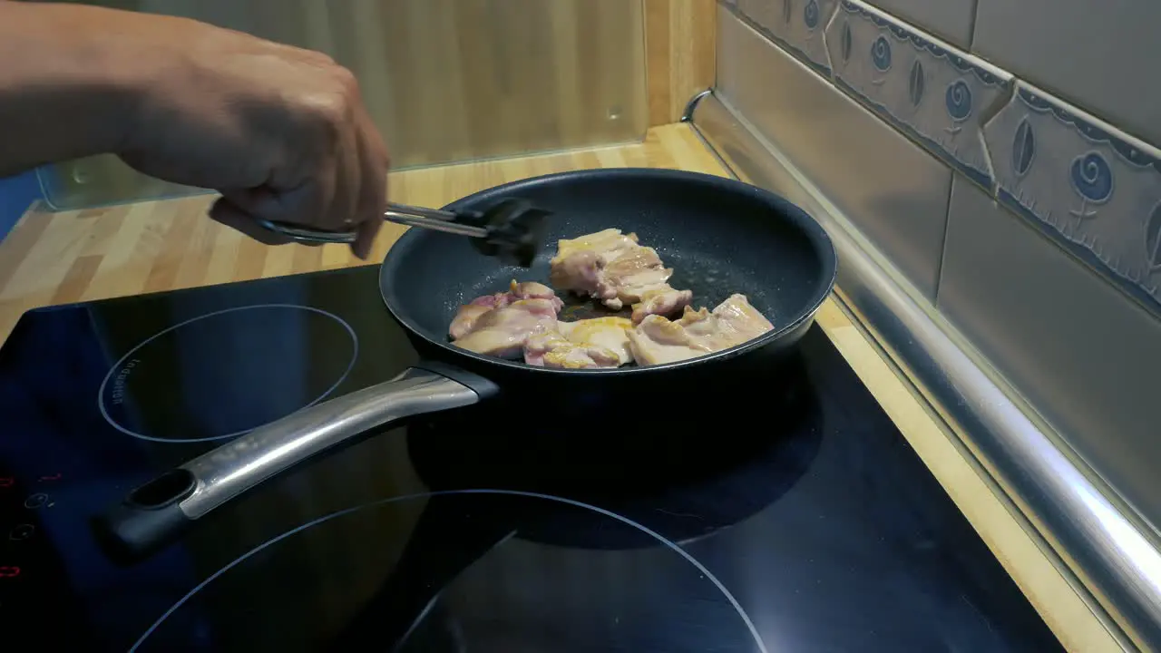 A man´s arms turning around a chicken drumsticks fillets in a pan