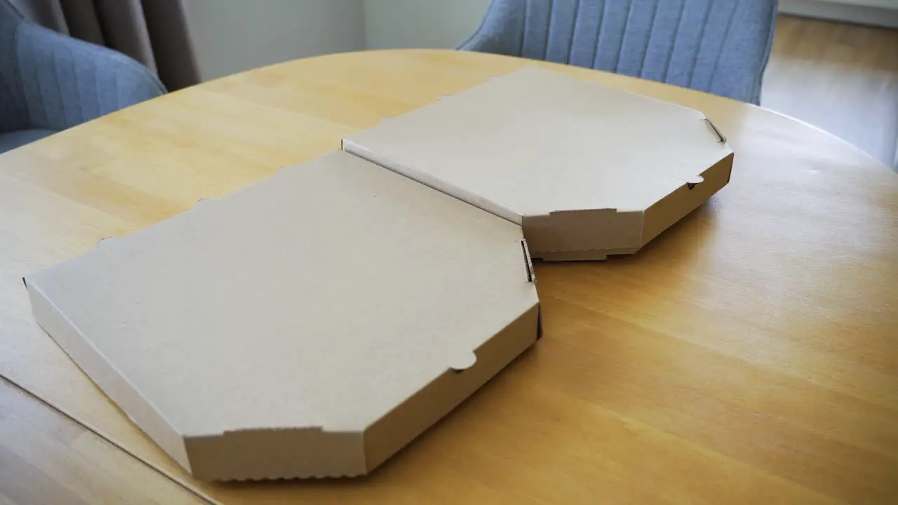 the handheld shot of man's hand opening delivered Italian pizzas in a cardboard box on the table at home