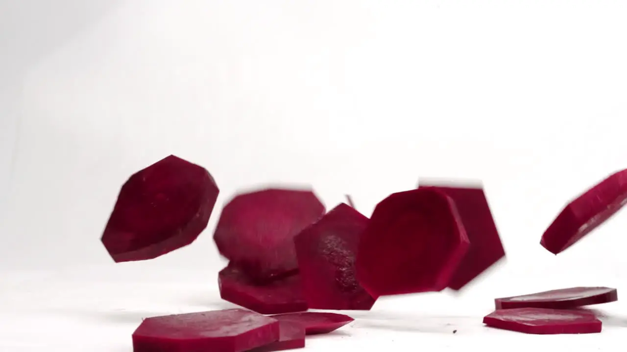 Beet slices falling and bouncing on white backdrop in 4k slow motion