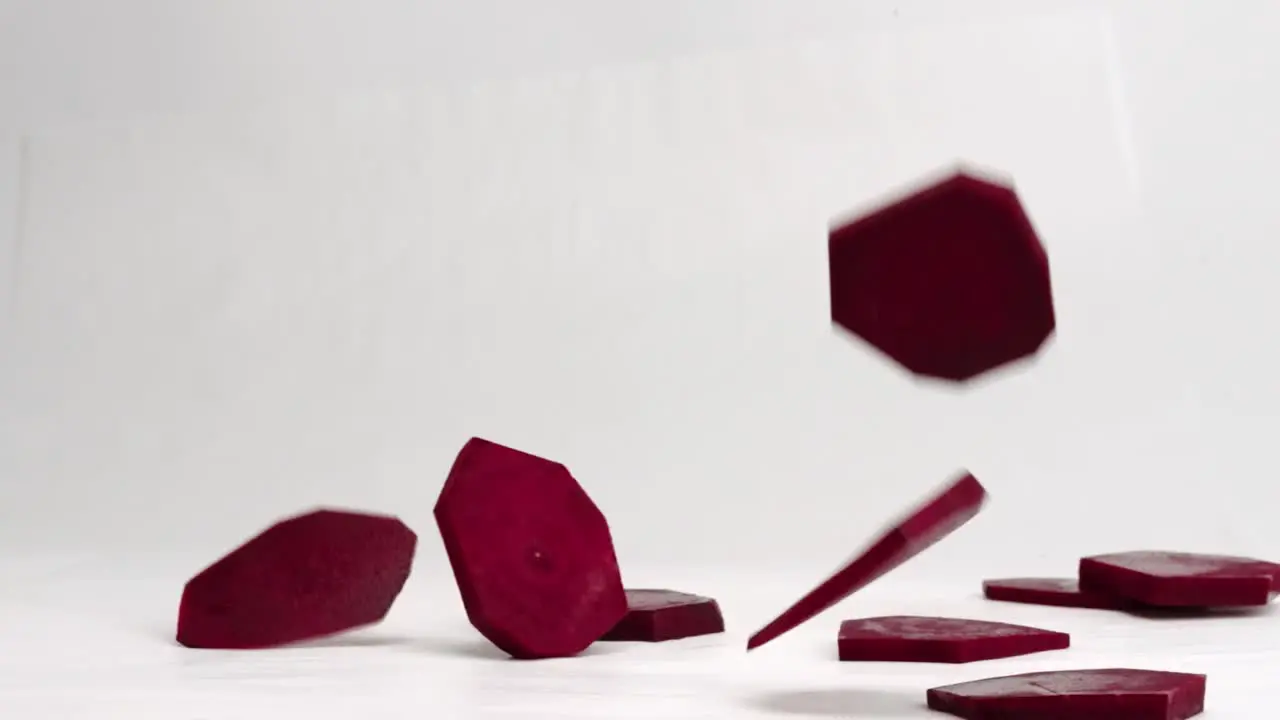 Geometric beet slices falling and bouncing in slow motion on a white backdrop in 4k