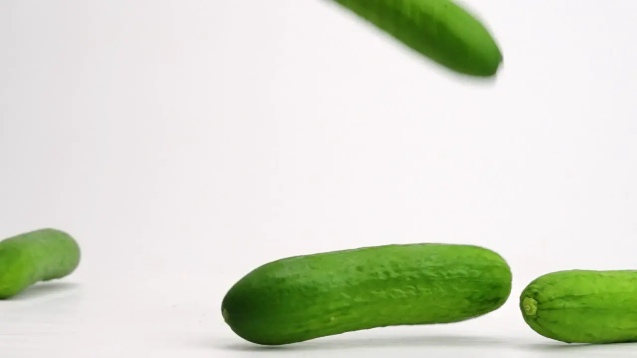 Whole Persian mini cucumbers bouncing onto white table top and rolling around in slow motion