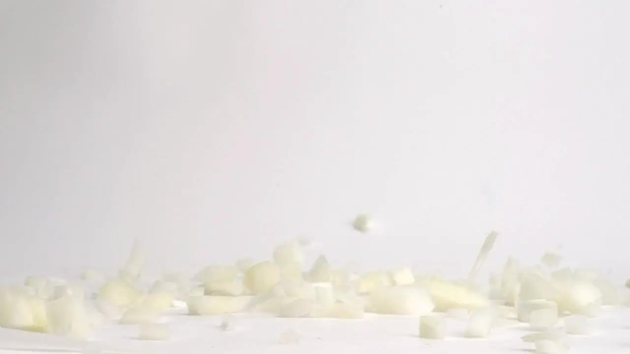 Diced white onion pieces falling and bouncing on white table top in slow motion