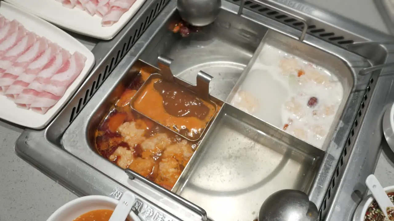 panning view of szechuan hotpot style with boiling soup and pork sliced on table