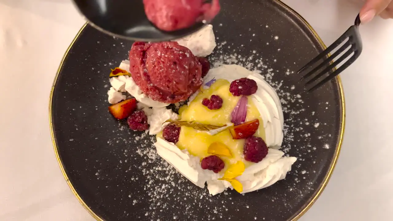 Delicious dessert on a plate with fruits and creme fresh person eating with a spoon and fork