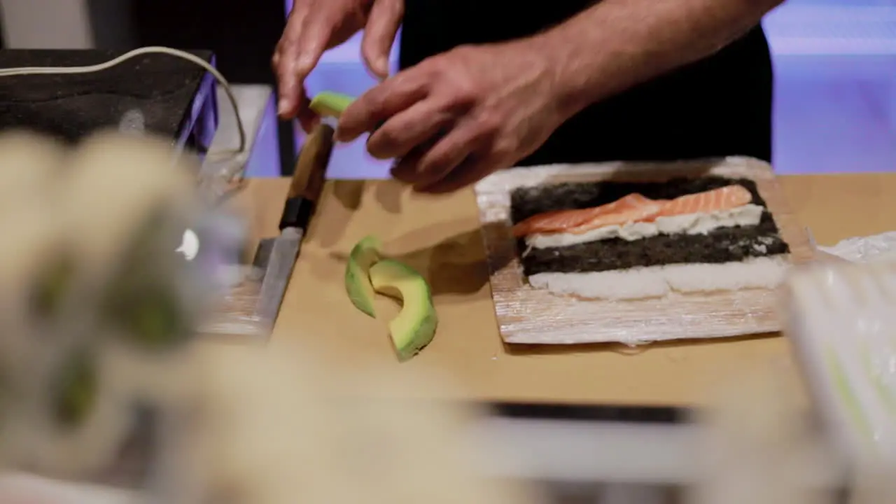 Detail of hands preparing a sushi roll with rice avocado and salmon