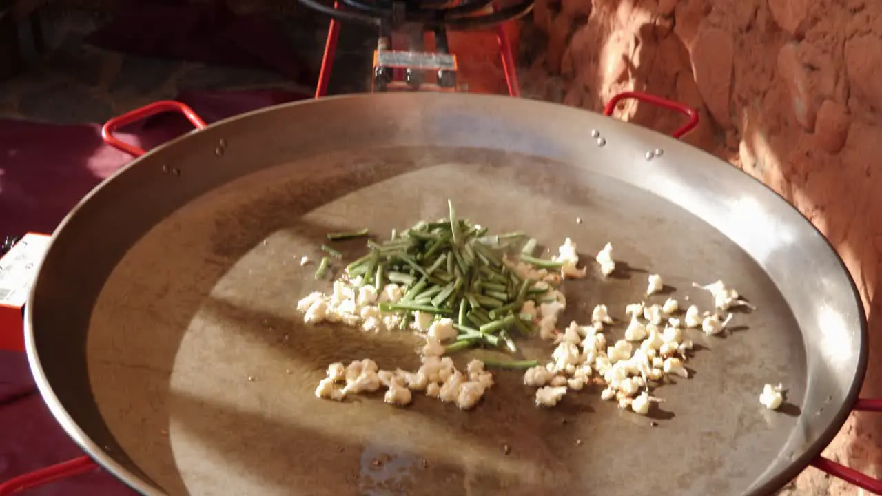 A shot of a paella pan outdoors being used near another in a spanish house yard