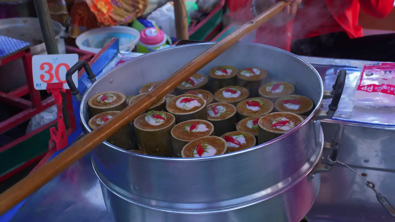 Static close-up of a pot of dim sum-like Thai food and a local vendor handing out the packs