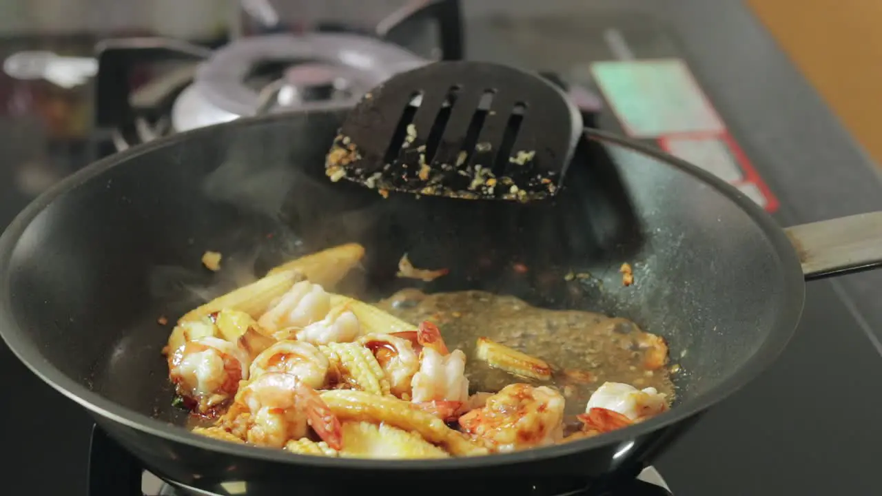 Woman is adding water to frying shrimps with chili and garlic in a hot frying pan