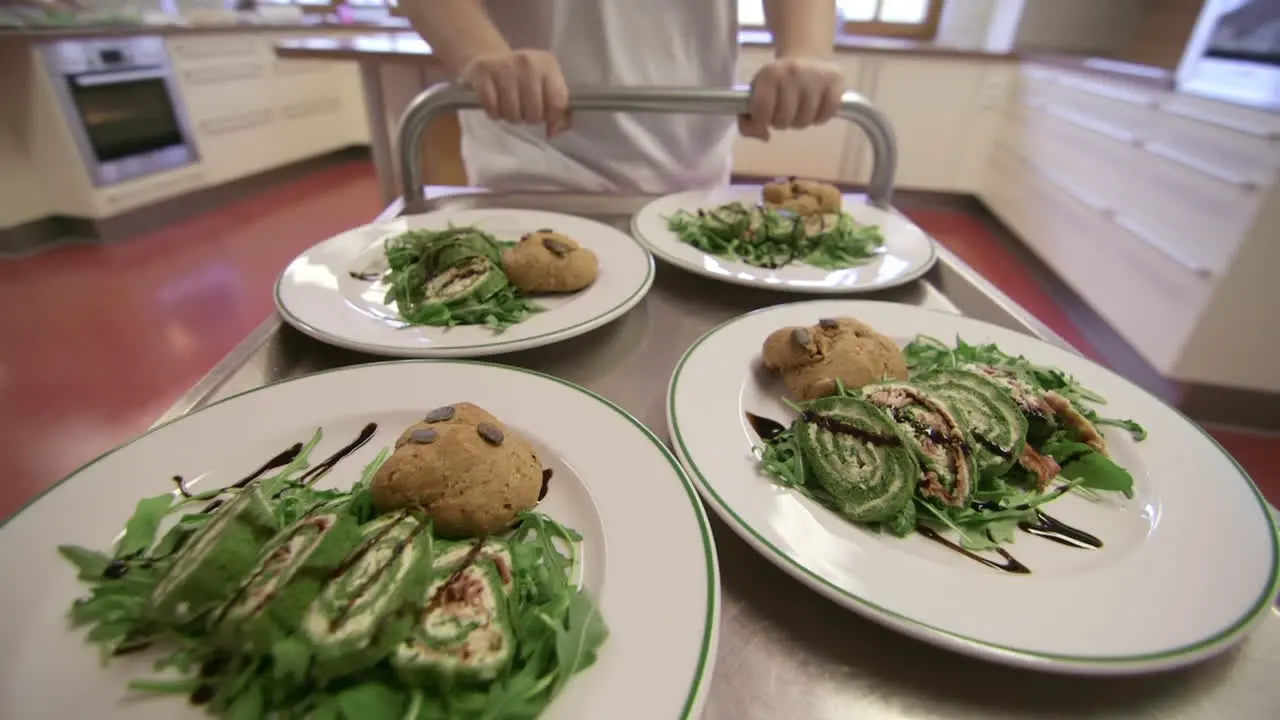 Meals moving through restaurant kitchen on steel cart pushed by kitchen assistant