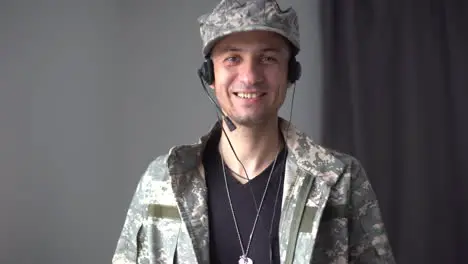 Cinematic shot of young happy smiling male soldier in camouflage military uniform is making technology video call to her family or friends just turn back home after mission