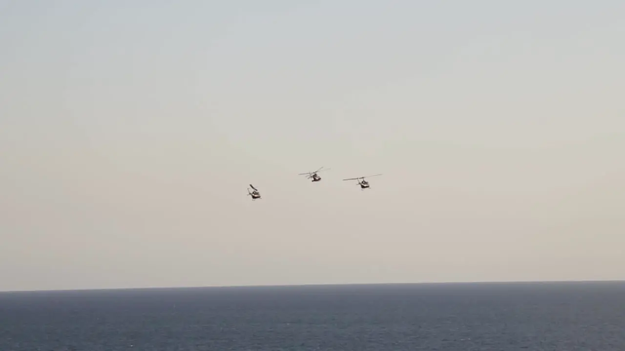 wide shot from far away of helicopters in aerial show with sea bottom