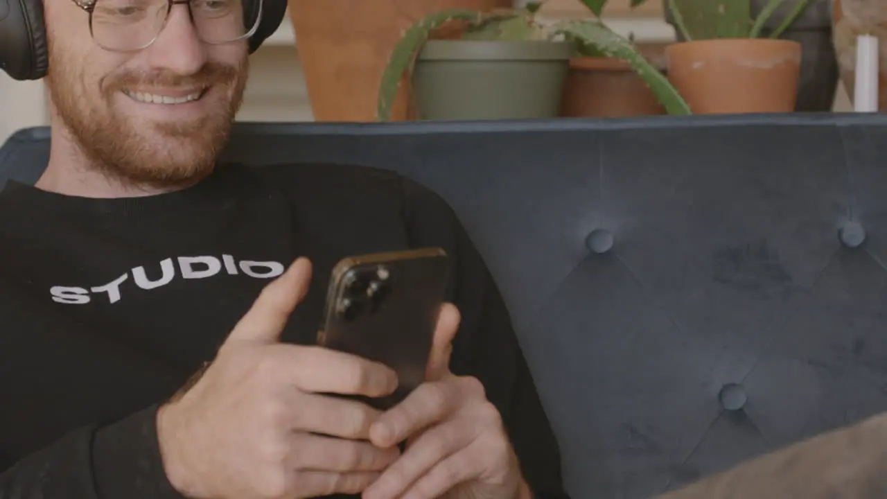 Medium close front angle of a man sitting on a couch scrolling and swiping and typing on an Iphone