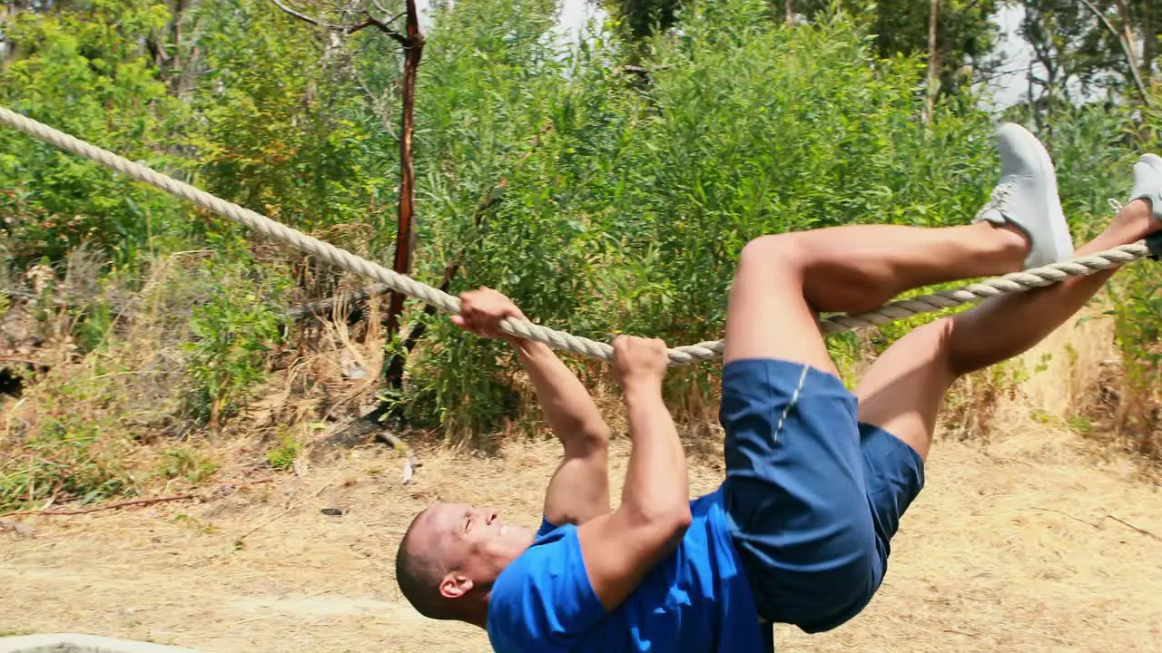 Fit man practicing rope climbing during obstacle course