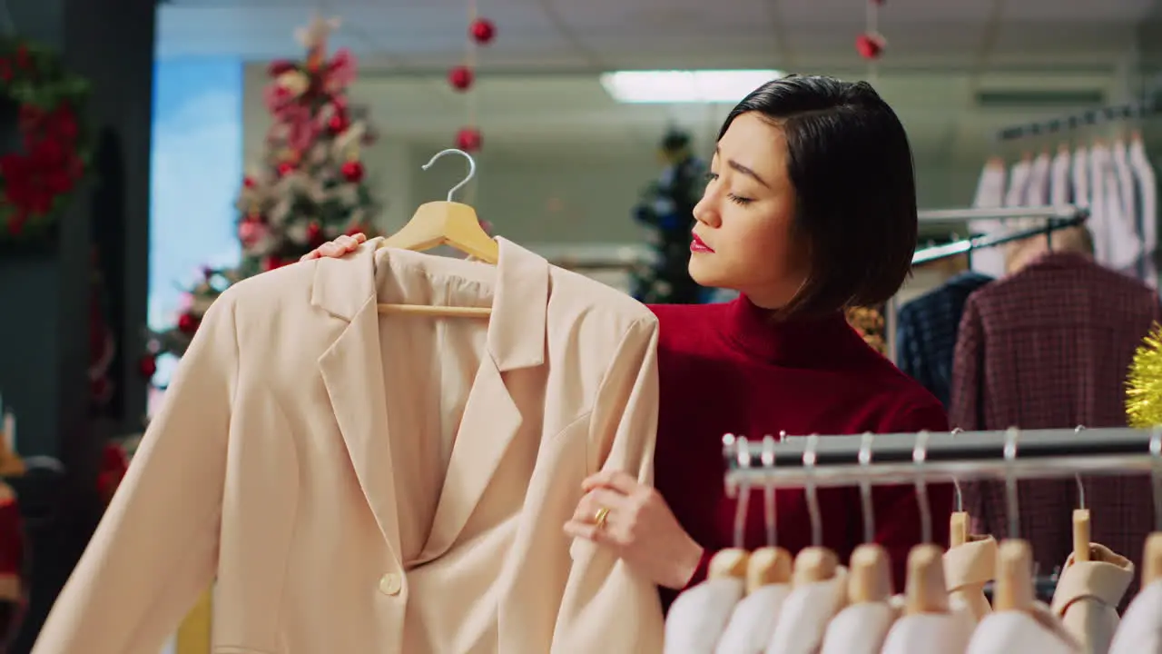 Portrait of happy woman browsing through elegant blazers on racks in Christmas adorn clothing store during winter holiday season Smiling client checking fashion boutique items