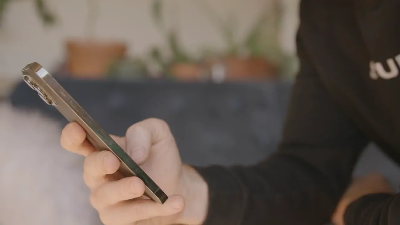 Side angle of a man scrolling and swiping and typing on an Iphone with a couch in the background