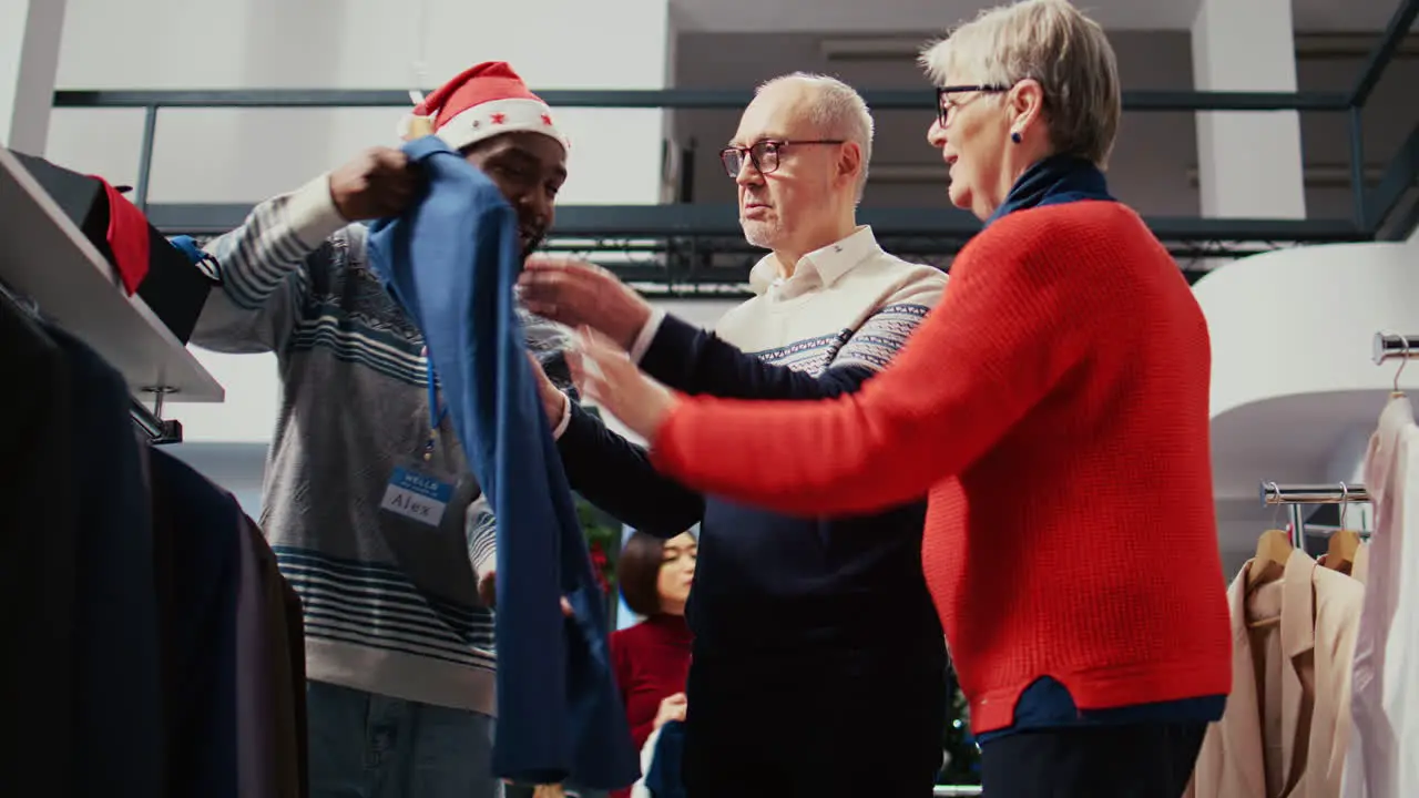 Elderly couple in festive adorn shopping mall fashion boutique being helped by friendly retail assistant with finding ideal outfit during Chrismas holiday season promotional sales