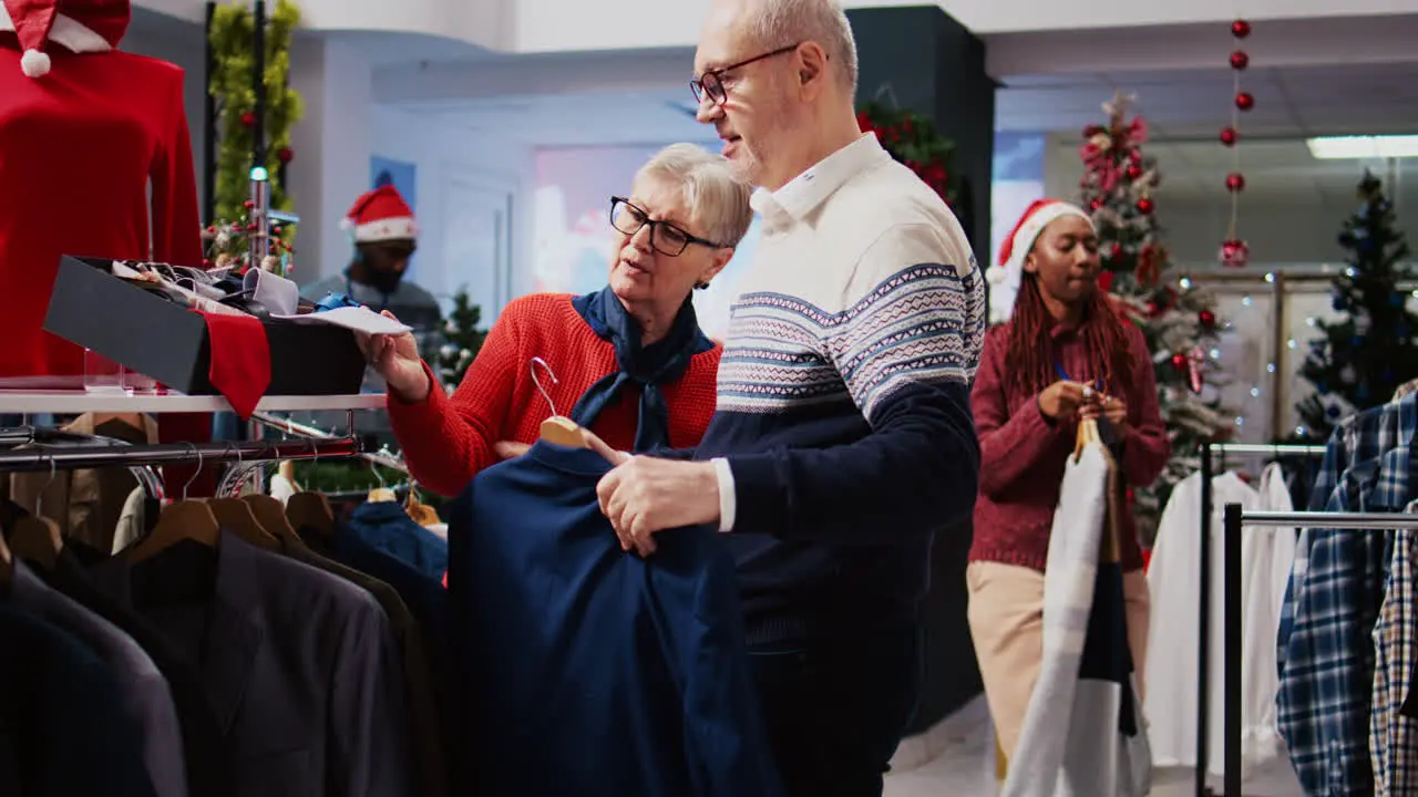 Senior couple browsing through clothes racks in festive adorn clothing store during Christmas shopping spree Old clients planning to purchase formal attire enjoying holidays promotional sales