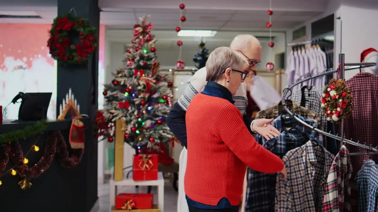 Tracking shot of elderly couple browsing through shirts in festive decorated clothing store during Christmas shopping spree Senior huband and wife looking to buy formal attire