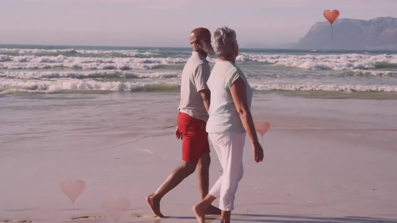 Animation of hearts over senior african american couple walking on sunny beach