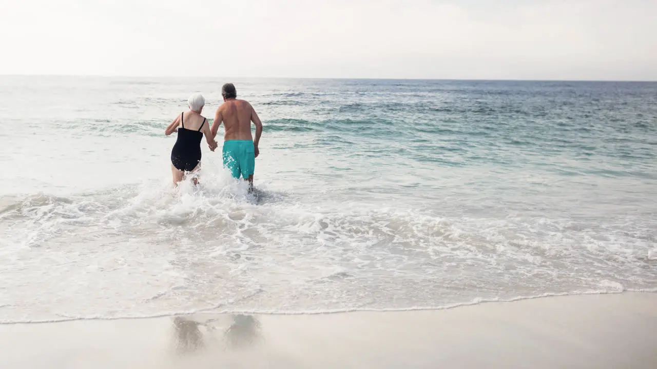 Caucasian senior couple on holiday holding hands walking in sea