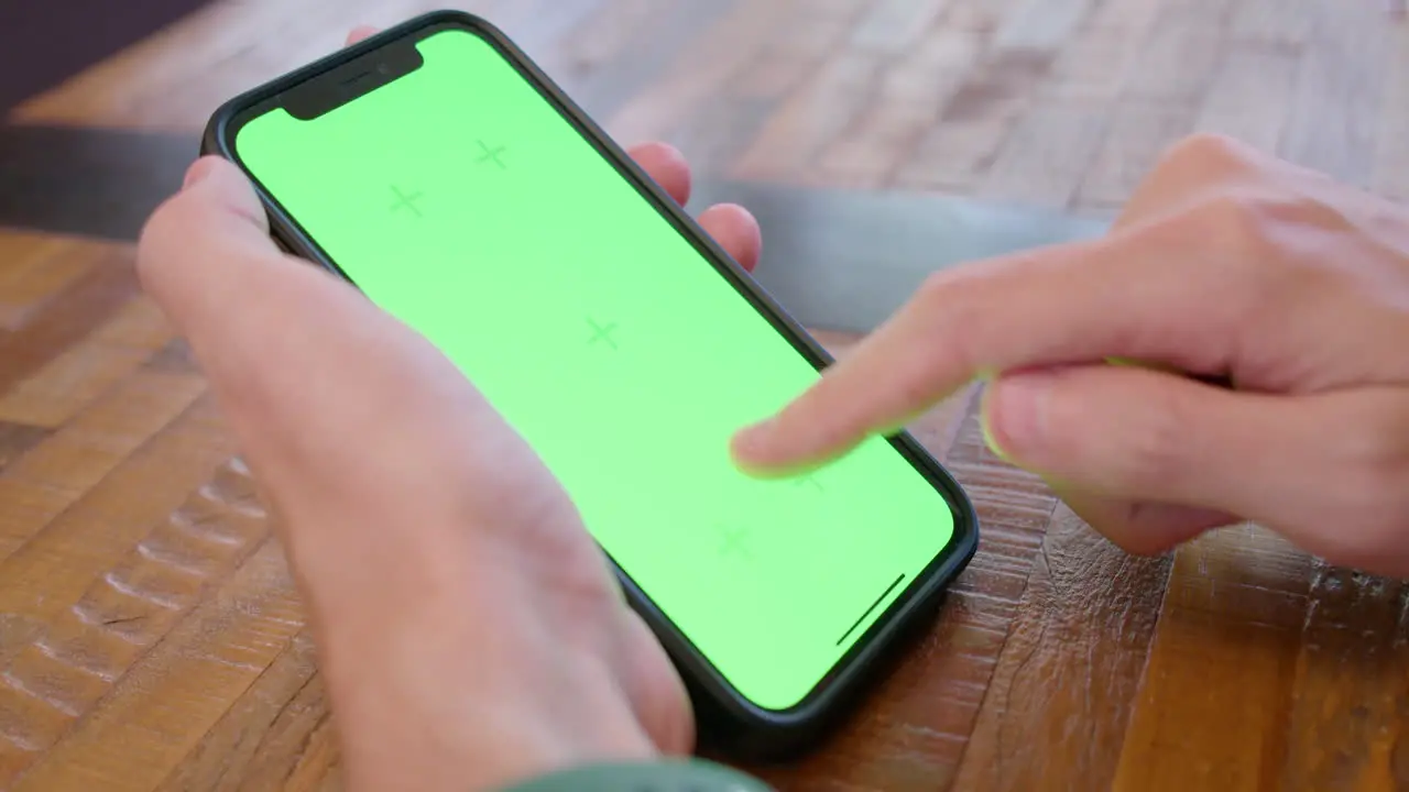 Cinematic shot of person holding an iPhone with green screen display tapping and swiping on the screen