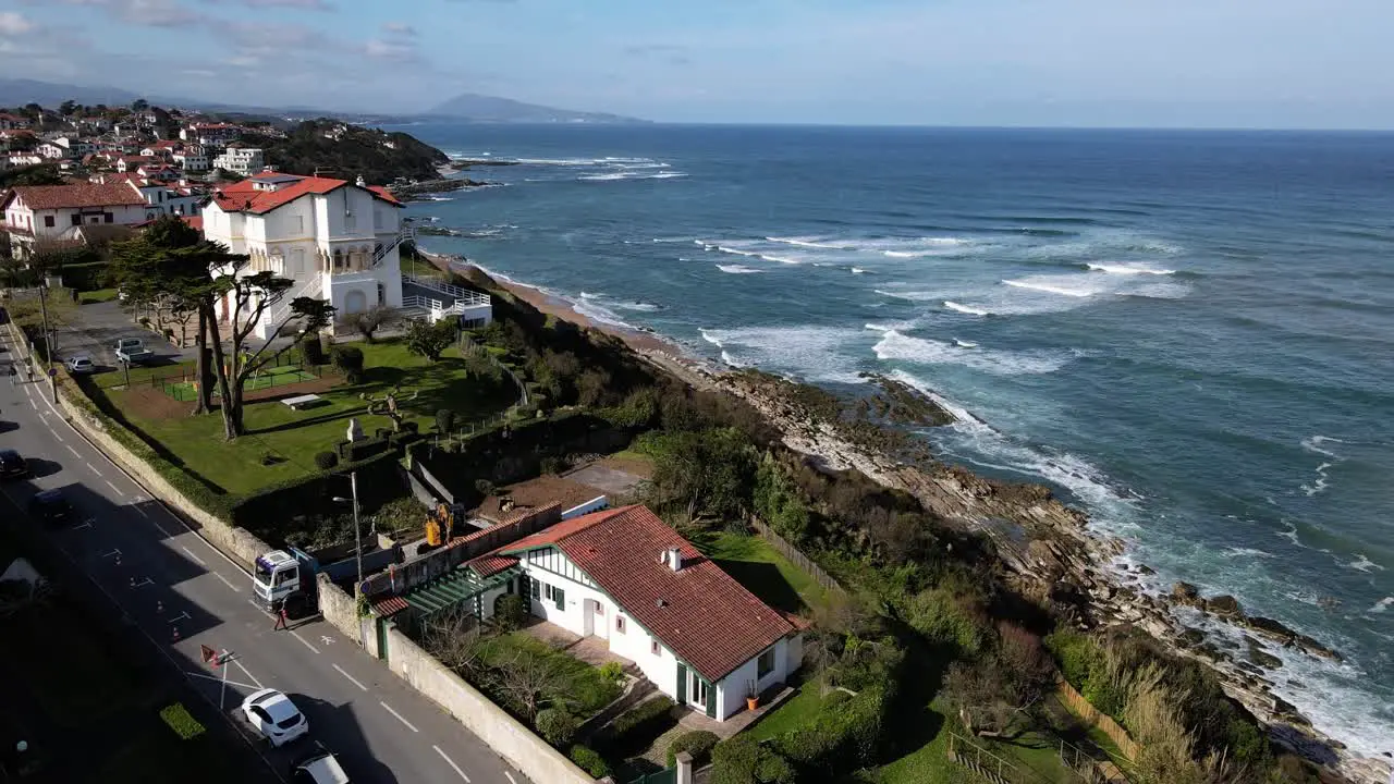 Drone flys over French Basque Country town Bidart with many basque homes along the coastline and Parlamentia surf break with waves crashing on the shore