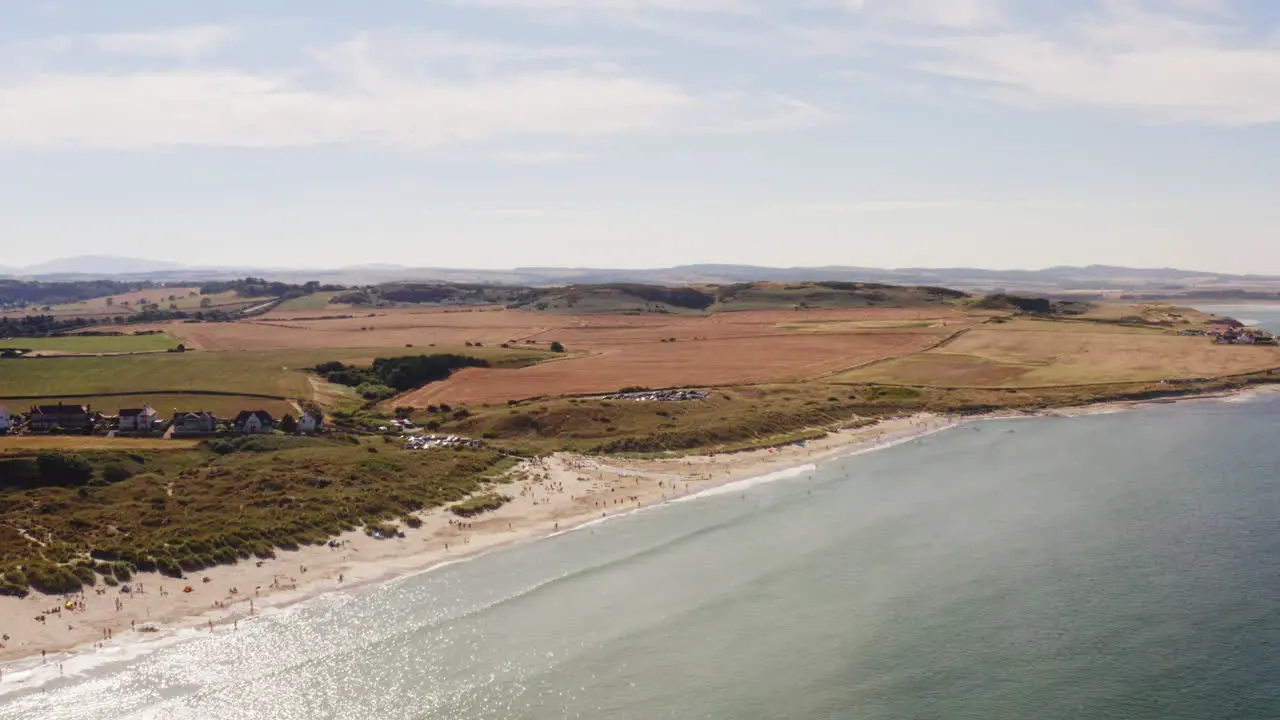 Aerial shot of a British beach in the summertime holidaymakers relax and enjoy the quiet beach surrounded by green fields