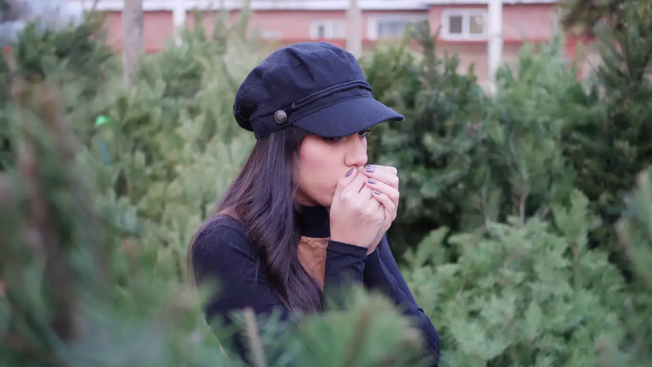 A young woman shopping for a Christmas tree and looking cold in the winter holiday season