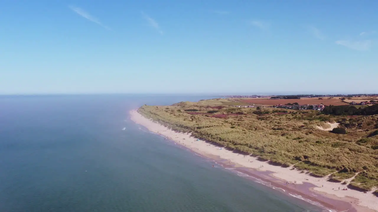 Aerial shot from high above rising over a British beach on a scorching summer day while families play below