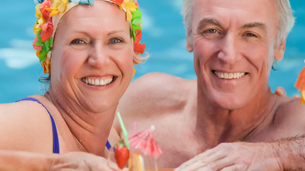 Portrait of caucasian senior couple on holiday with cocktail in swimming pool