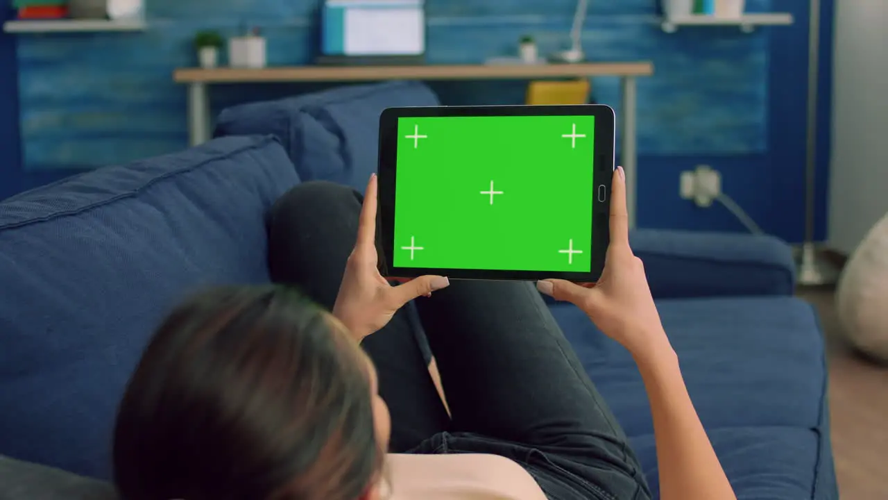 Over the shoulder view of casual woman sitting on sofa using tablet computer