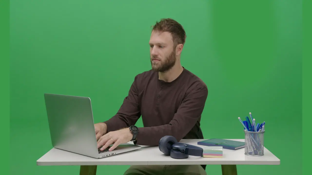 Uoung Caucasian man is using his laptop in a frontal view captured in a portrait shot with a green screen or chroma key