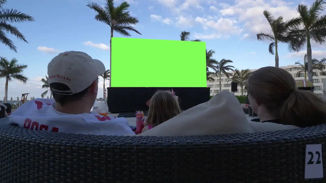 Family of 3 watching large outdoor green screen at a tropical resort