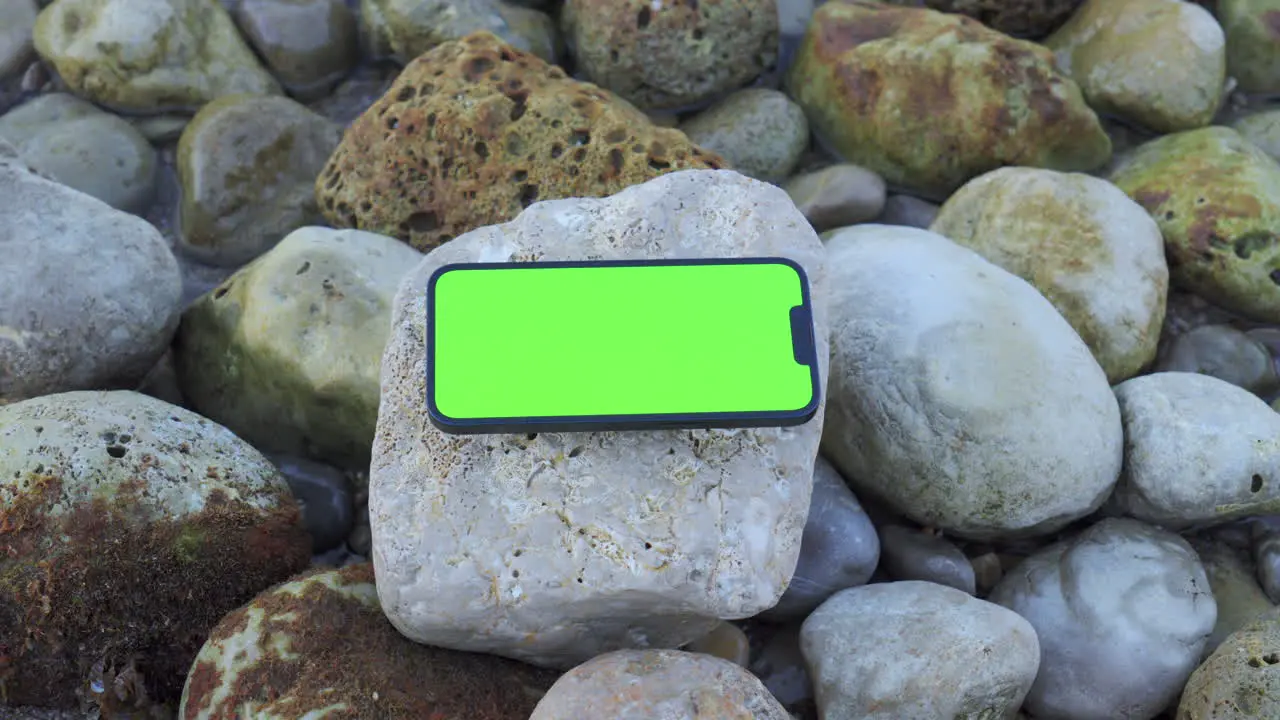 iPhone 14 with Green Screen Resting on Rocks by the Morning Sea