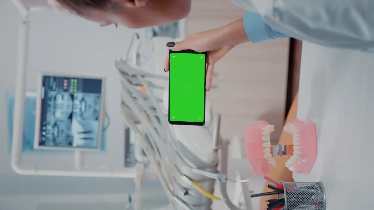 Vertical video Dentist looking at mobile phone with green screen