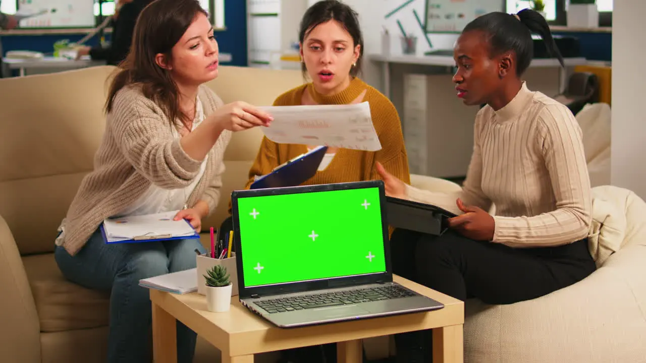 Diverse women sitting at table discussing strategy with green screen laptop