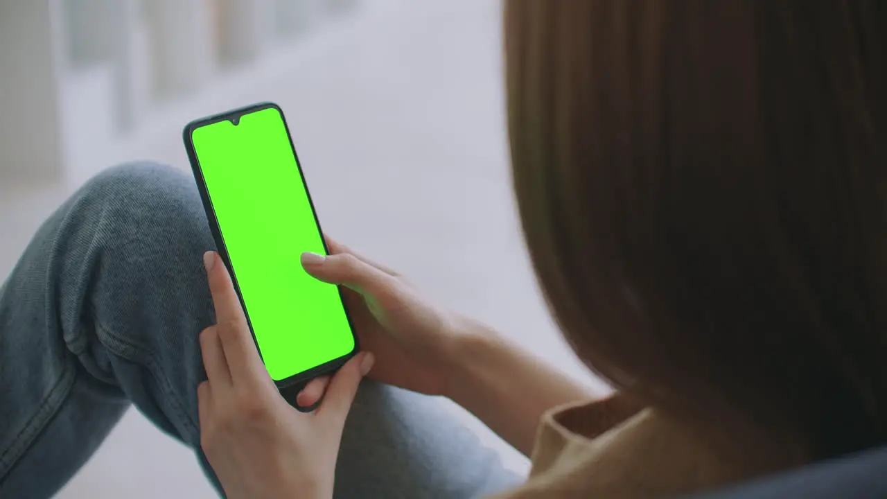 Point of View of Woman at Modern Room Sitting on a Chair Using Phone With Green Mock-up Screen Chroma Key Surfing Internet Watching Content Videos Blogs Tapping on Center Screen