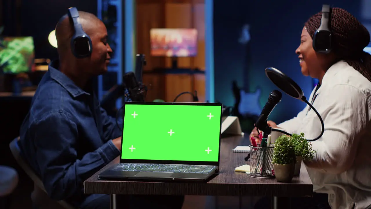 Green screen laptop next to man on podcast discussing with guest during marathon stream