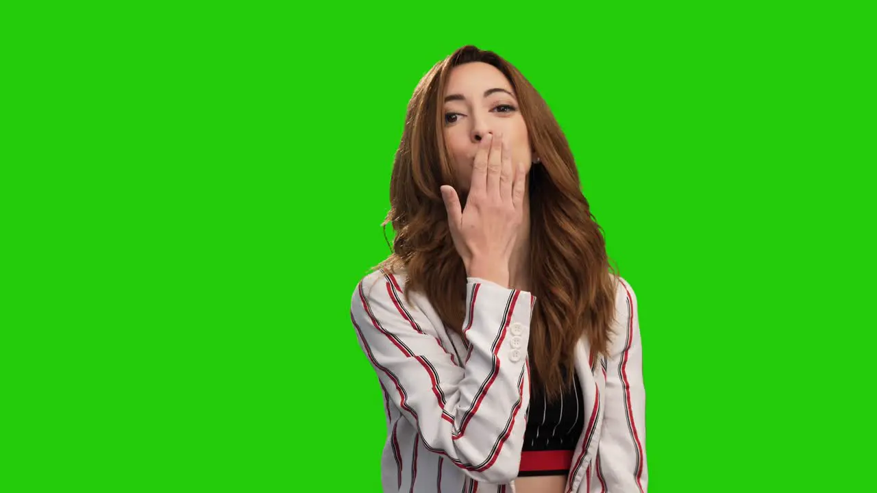 Pretty young woman poses on green screen showing heart gesture and blowing kiss