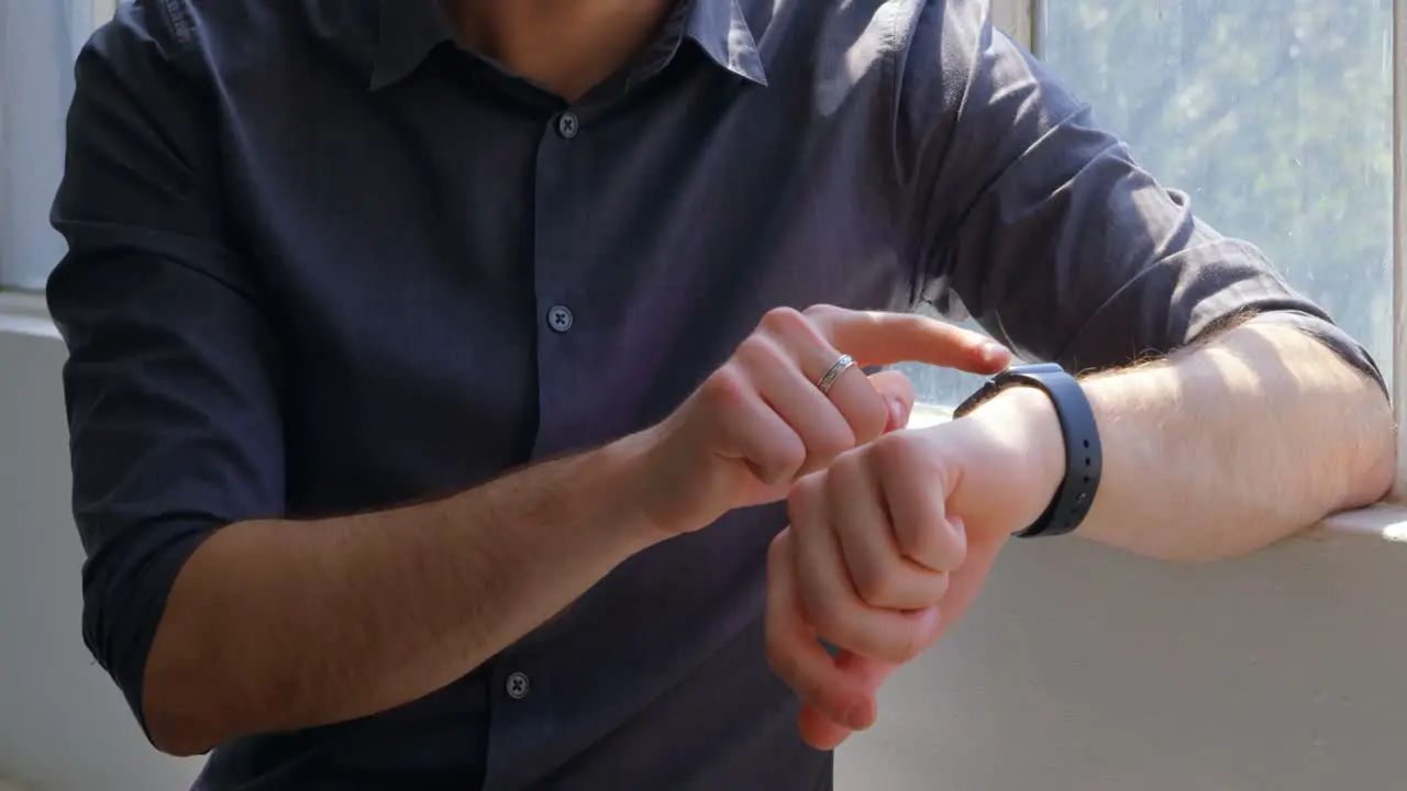 Front view of young businessman using smartwatch and sitting near window of modern office 4k