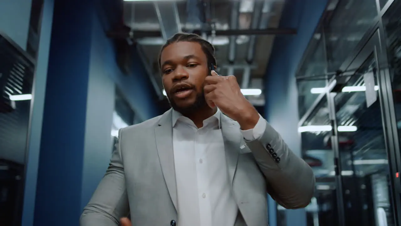 Focused afro man speaking on phone in office Man using smartphone in corridor