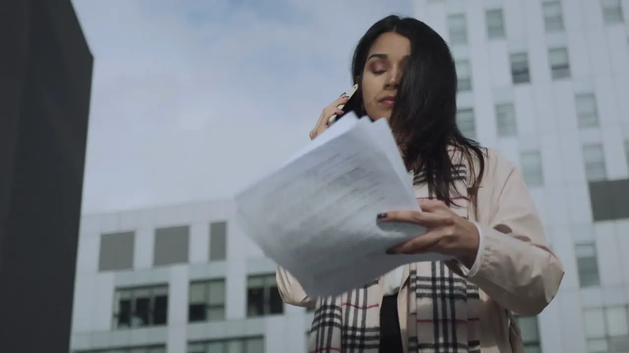 Businesswoman talking smartphone at street Busy girl reading documents outdoors