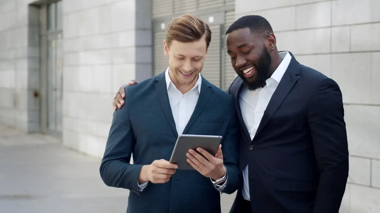 Two happy businessmen reading good news on digital tablet in modern city