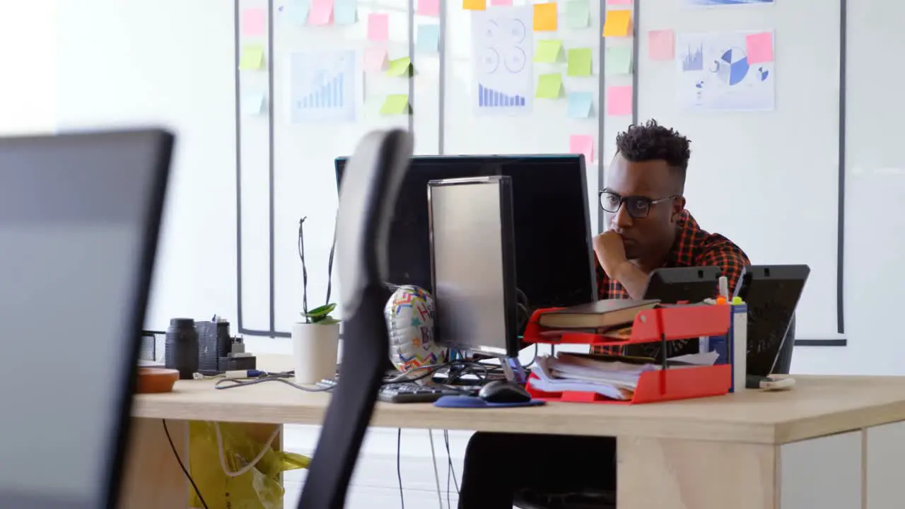 Front view of thoughtful young black businessman working and sitting at desk in a modern office 4k